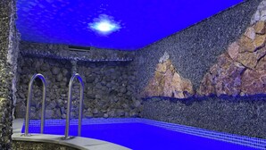 Ein Schwimmbecken mit einer Steinwand im Hintergrund, einer integrierten Sitzbank und einer Decke mit blauem Himmel-Motiv.