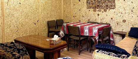A cozy room with a wooden ceiling, a chandelier, a dining table with chairs, and a patterned wall.