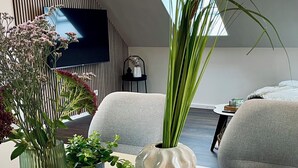 A modern living room with a large TV, a sofa, and a coffee table with decorative plants. - Holiday apartment in the Eifel - for those seeking peace and quiet and nature lovers directly on the cycle path (Arzfeld)