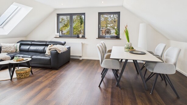 A modern loft apartment with a black leather sofa, a dining table with chairs, and two windows with views of trees. - Holiday apartment in the Eifel - for those seeking peace and quiet and nature lovers directly on the cycle path (Arzfeld)