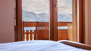 A room with a bed and a wooden chair facing a mountain view through a window. - Victoria II E7 - 10 pers - at the foot of the slopes (Haute-Nendaz)