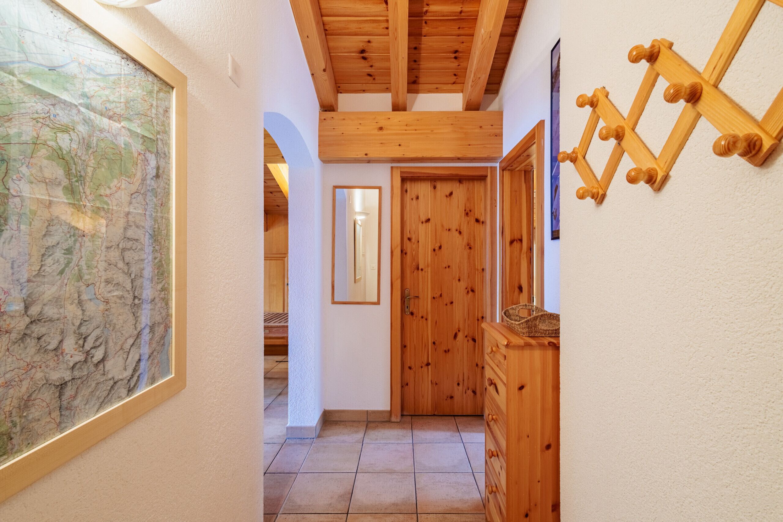 Ein Korridor mit Holzbalken, einer Karte an der Wand, einer Holztür und einem Schrank.