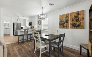 A modern kitchen with white cabinets, a stainless steel refrigerator, and a dining area with a dark wooden table and chairs. - Seagrove -  Community Pool - Steps To The Beach (Santa Rosa Beach)