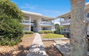 A two-story building with a central courtyard, a wooden pathway, and a palm tree. - Seagrove -  Community Pool - Steps To The Beach (Santa Rosa Beach)