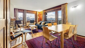 A modern living room with a wooden floor, a sofa, a dining table with chairs, and large windows with a mountain view. - Eden Roc 1 - 4 pers - near the slopes (Haute-Nendaz)
