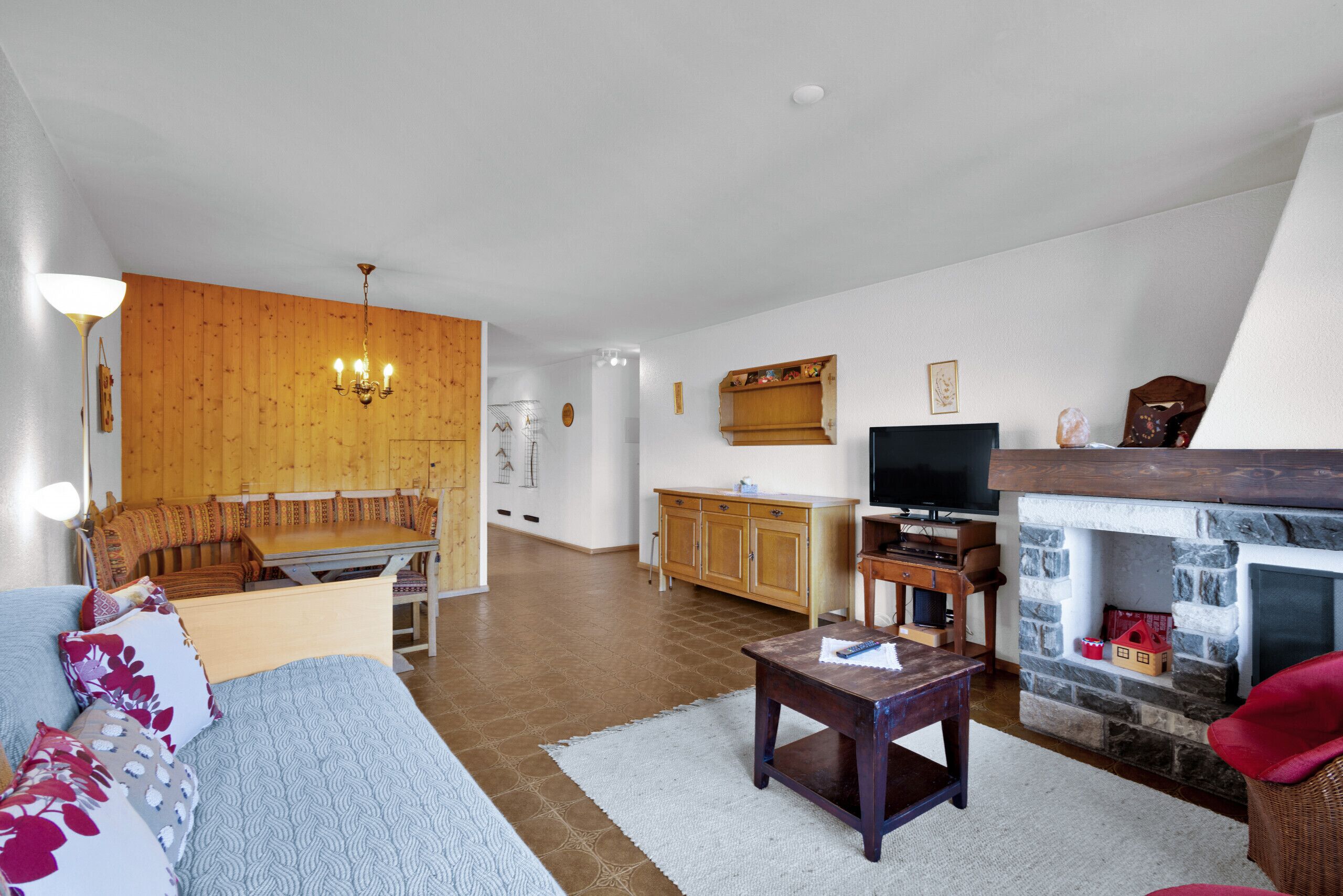 Een ruime woonkamer met een houten bank, een televisie, een open haard en een eethoek met een houten tafel en stoelen.