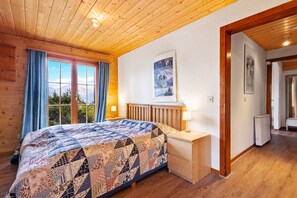 A wooden-paneled bedroom with a large bed, a nightstand, a dresser, and a window with curtains. - Marcotte - 8 pers - beautiful view (Haute-Nendaz)