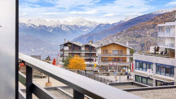 Ein Hotel mit Blick auf schneebedeckte Berge, ein Holzhaus und ein modernes Gebäude mit Balkonen.