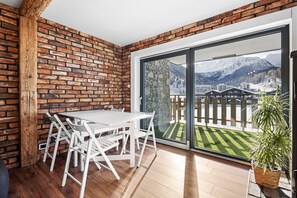 A room with a white table and chairs, a brick wall, and a large sliding glass door leading to a balcony with a mountain view. - Dents-Rousses D2 - 4 people - Siviez (Siviez)