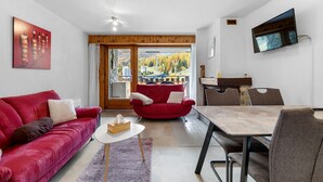 A modern living room with a red sofa, a dining table, and a TV mounted on the wall. - Dents-Rousses D4 - 4 pers - ski In&Out (Siviez)