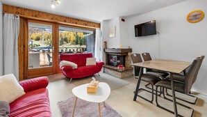A modern living room with a red sofa, a wooden dining table, and a fireplace. - Dents-Rousses D4 - 4 pers - ski In&Out (Siviez)