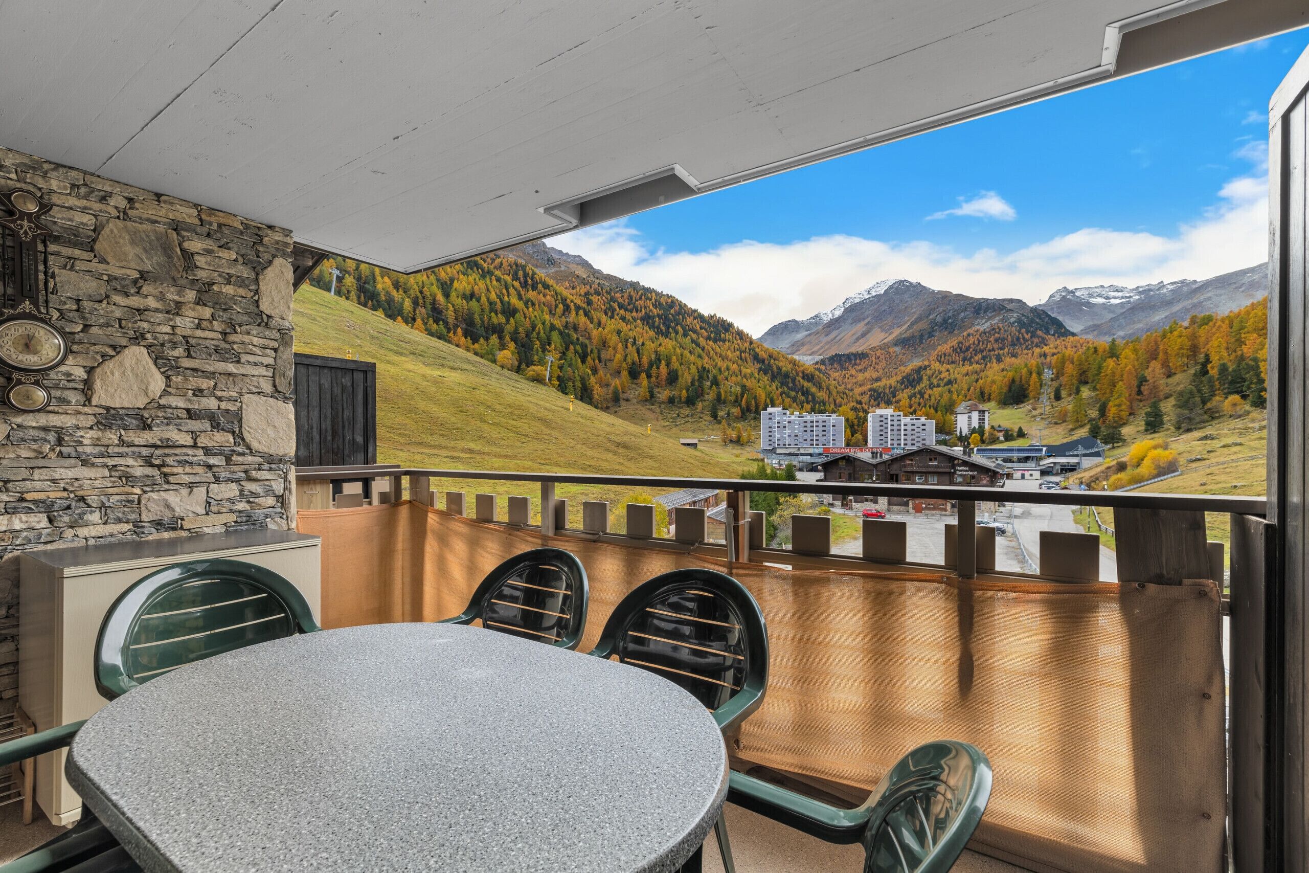 A balcony with a table and chairs, overlooking a mountainous landscape with buildings.