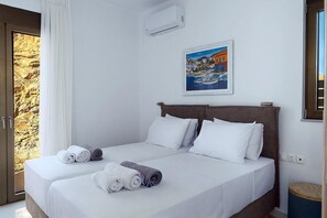 A double bed with white linens, a painting of a coastal scene, and a stone wall visible through an open door. - 3 Bedroom Villa Chara (Agia Pelagia)