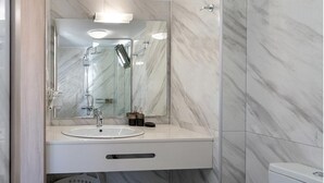 Ein Badezimmer mit Marmorwand, Waschbecken, Spiegel, Dusche und Toilette.