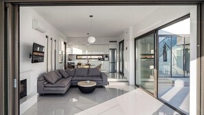 Ein modernes Wohnzimmer mit einem grauen Ecksofa, einem runden Couchtisch und einer Glastür, die auf einen Balkon führt.