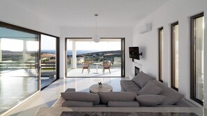 Ein modernes Wohnzimmer mit einer großen Couch, einem Couchtisch und Blick ins Freie durch große Fenster.