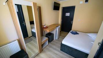 A compact room with a bed, a desk, a mirror, and a wardrobe.