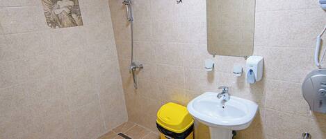 A bathroom with beige tiles, a yellow trash bin, a sink, and a shower.