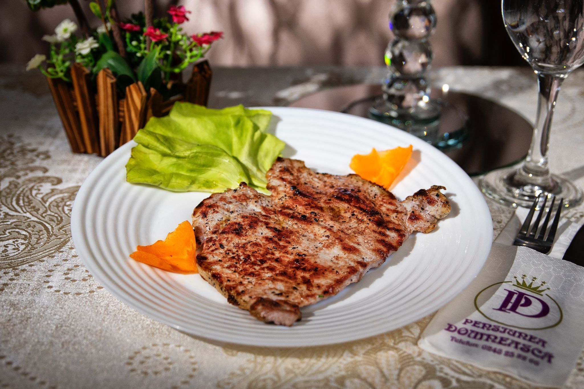 A plate with grilled meat, lettuce, and orange slices on a table with a lace tablecloth.