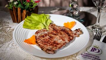 A plate with grilled meat, lettuce, and orange slices on a table with a lace tablecloth.