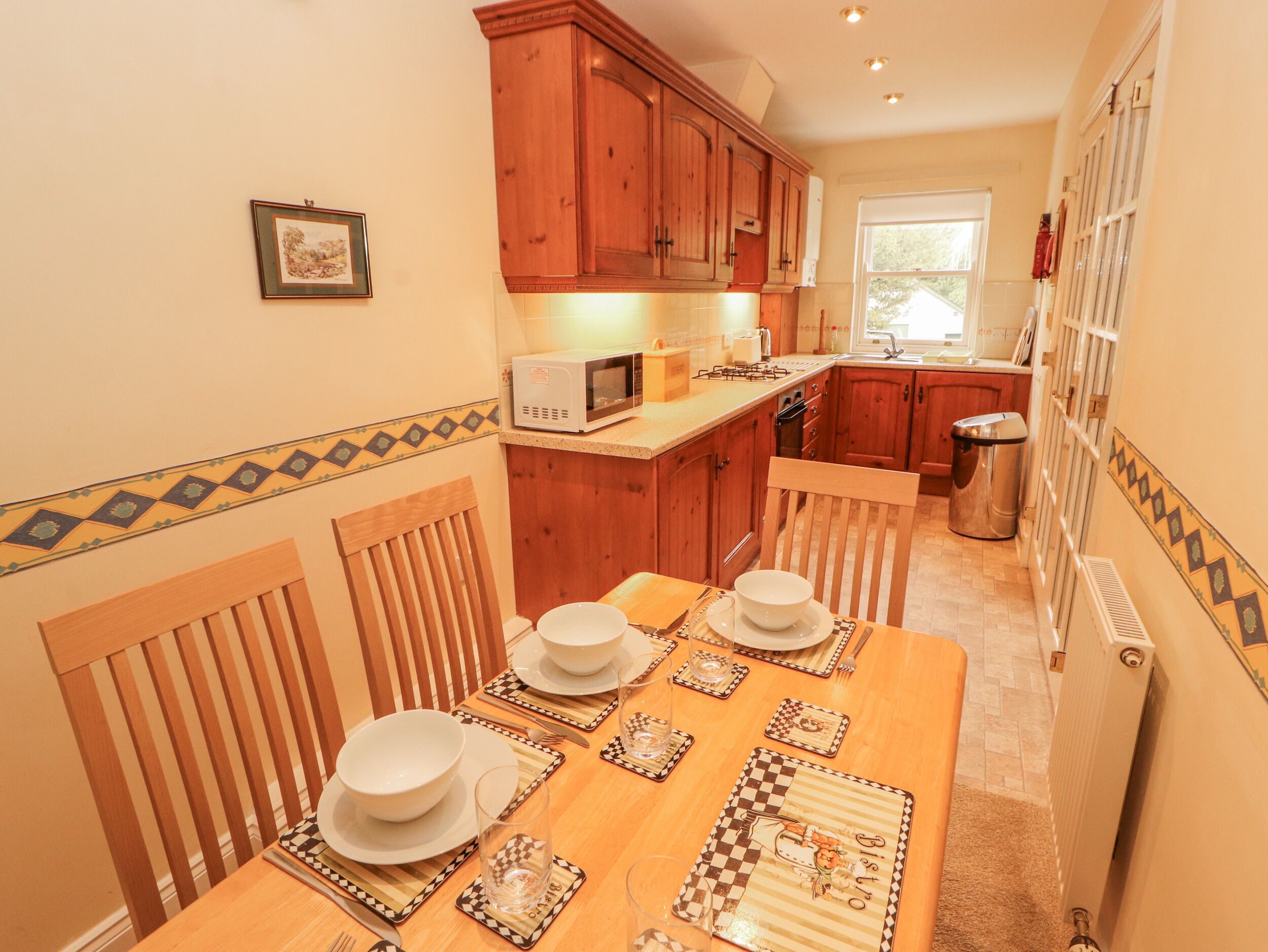 Cocina compacta con armarios de madera, microondas y una mesa para cuatro.