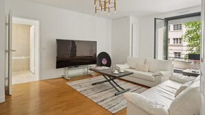A modern living room with a flat-screen TV, a coffee table, a sofa, and a large window. - Elegant New Apartment With Balcony in the 16th - M (Paris)