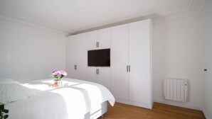 Une chambre à coucher avec un lit, un téléviseur fixé sur une armoire blanche et un radiateur au mur.