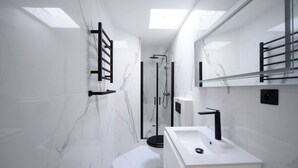 Une salle de bain moderne avec un mur en marbre blanc, une douche en verre et un lavabo blanc doté d’un robinet noir.