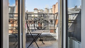 On aperçoit, à travers une porte vitrée, un balcon doté d’une rambarde en métal et d’un banc en bois.