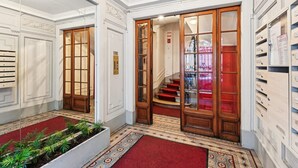 A hotel lobby with a red carpet, wooden doors, a staircase, and a wall of storage cabinets. - Charming Studio - Pereire - Lease Mobility (Paris)
