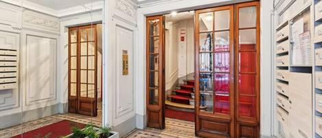 Un vestíbulo de hotel con alfombra roja, puertas de madera, una escalera y una pared de armarios.