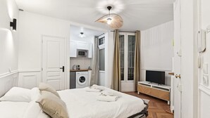 A hotel room with a bed, a TV, a washing machine, and a kitchenette. - Charming Studio - Pereire - Lease Mobility (Paris)