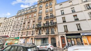 A multi-story building with balconies, storefronts, and parked cars. - Charming Studio - Pereire - Lease Mobility (Paris)
