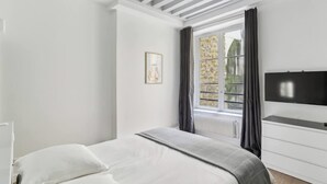 A bedroom with a bed, a dresser, a TV, and a window with curtains. - Exceptional Appt - Saint-germain- Mobility Lease (Paris)