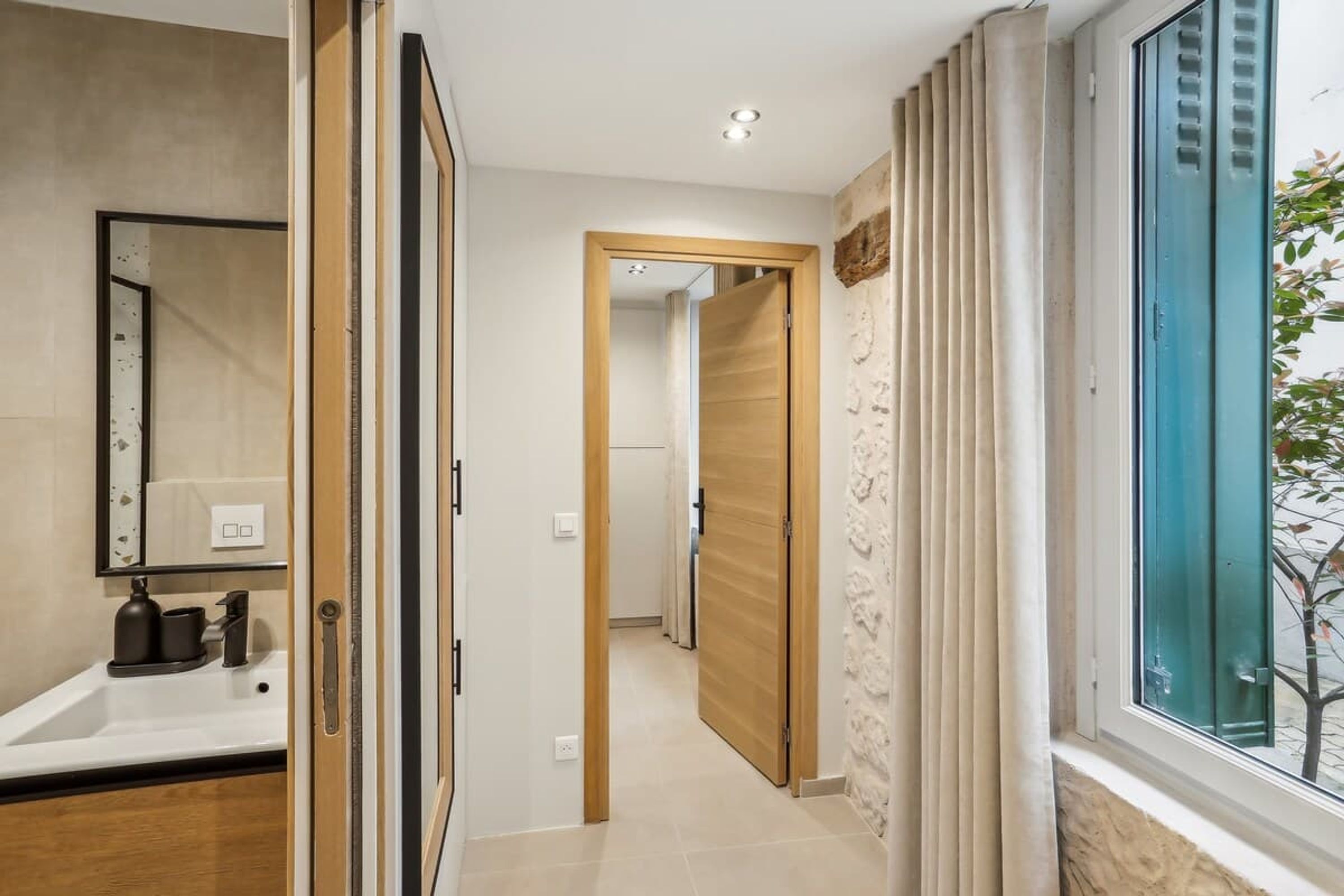 Une salle de bain moderne avec un grand miroir, un lavabo et une fenêtre avec des rideaux.