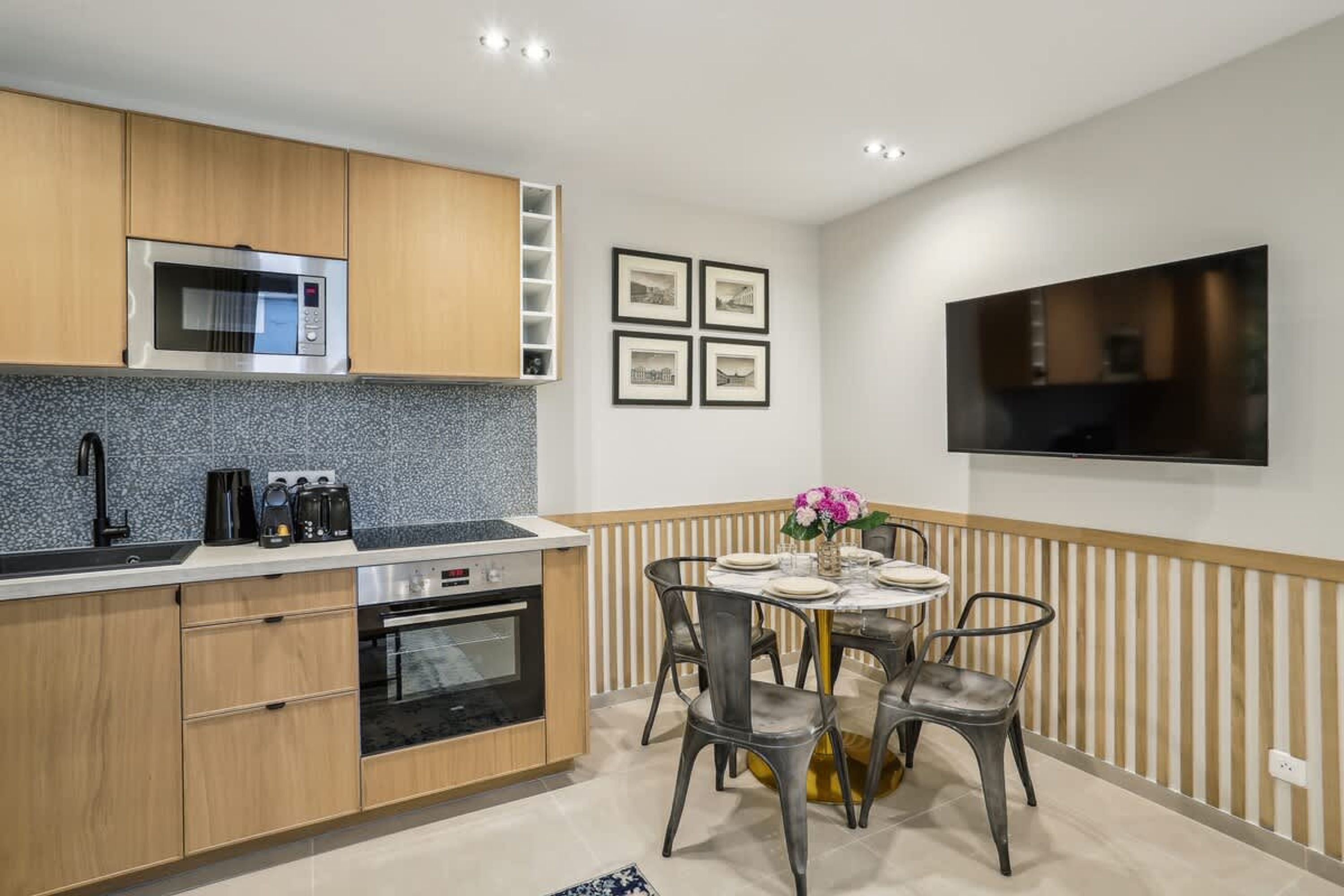 Een moderne keuken met houten kastjes, een magnetron, een fornuis en een eethoek met een tafel en stoelen.