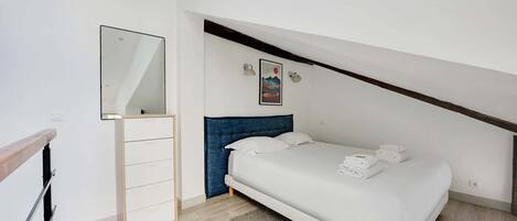 A bedroom with a bed, a dresser, a mirror, and a painting on the wall.