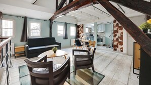 A spacious living area with a high ceiling, exposed wooden beams, a sofa, a dining table with chairs, and a kitchen in the background. - Authentic Apartment - 1BR 6P - Centre de Paris (Paris)