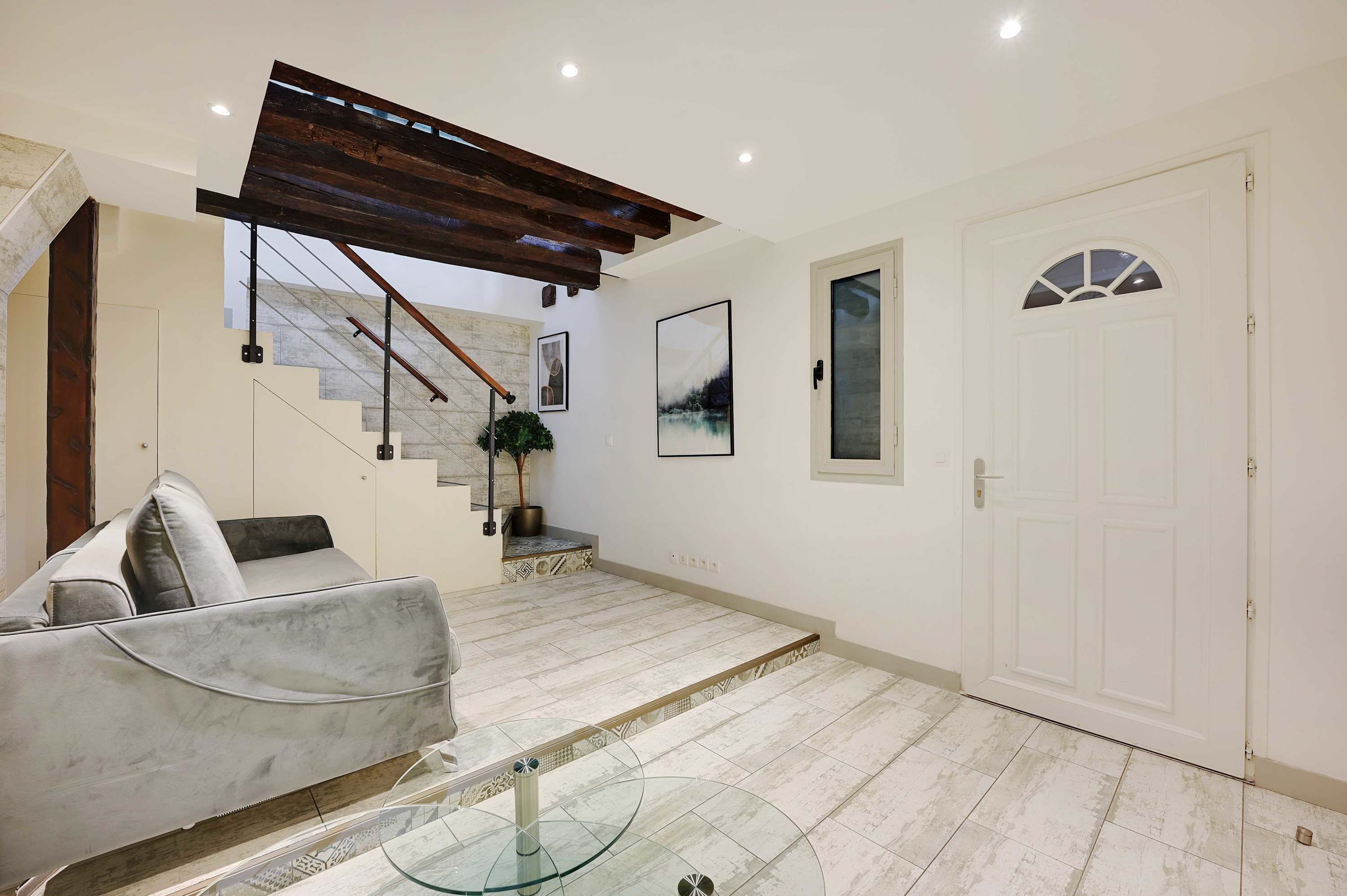 A modern interior with a staircase, a grey sofa, a glass table, and a white door.