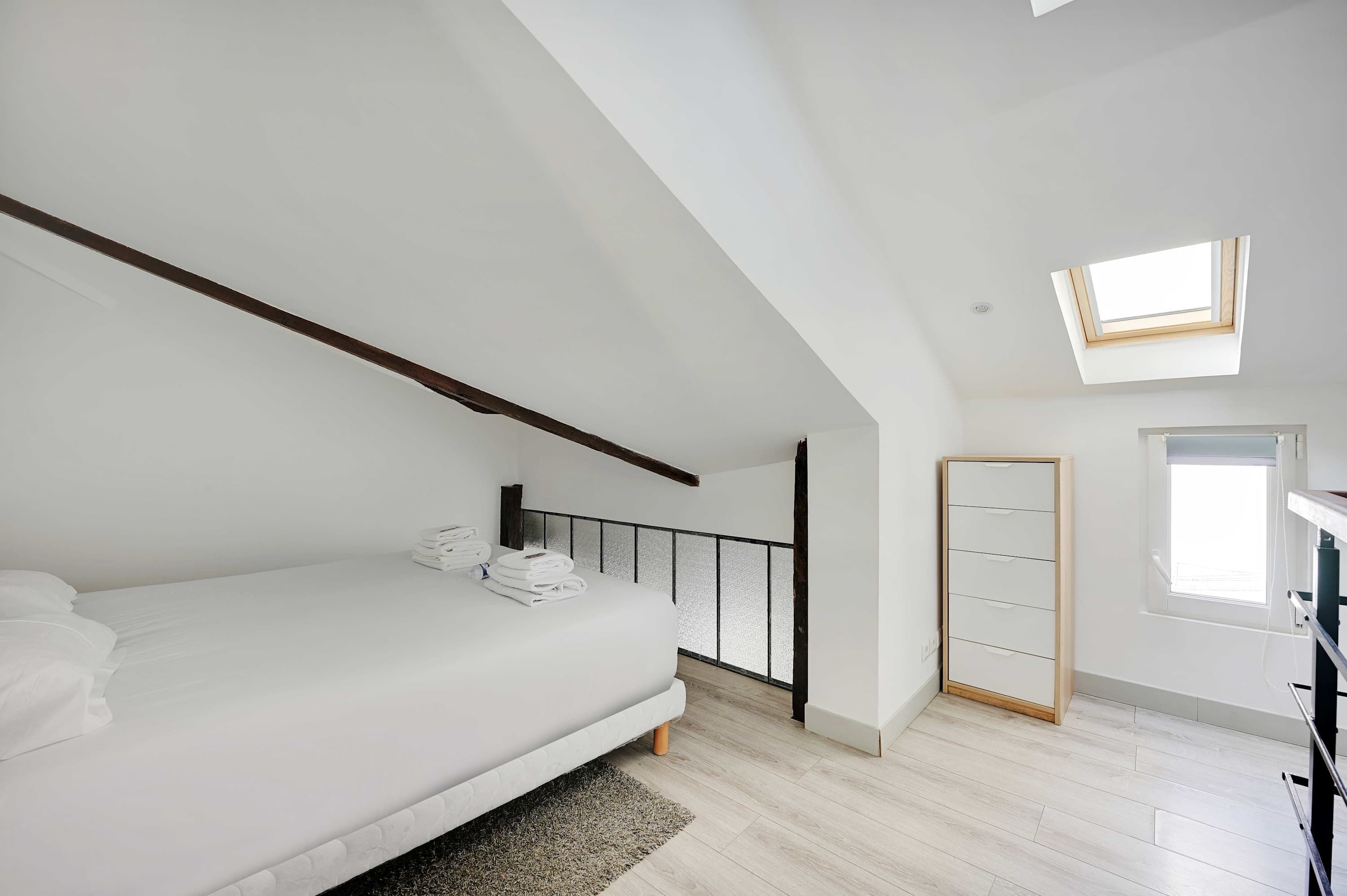 A bedroom with a bed, a skylight, a wardrobe, and a small window.