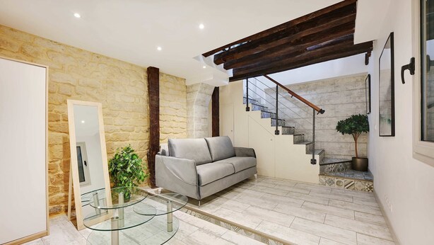 A modern living room with a stone wall, a gray sofa, a glass coffee table, and a staircase leading to an upper level. - Authentic Apartment - 1BR 6P - Centre de Paris (Paris)