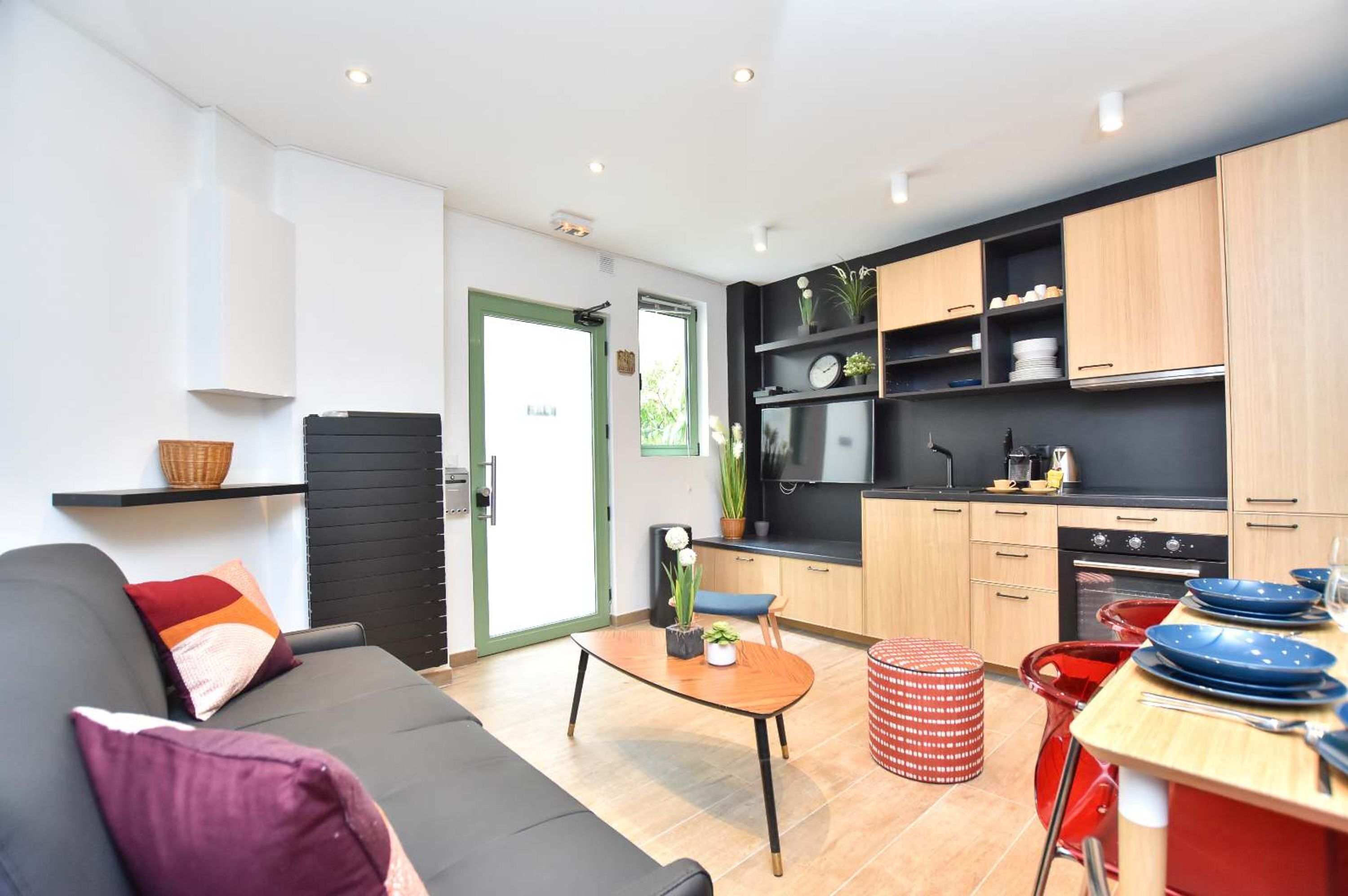 A modern living room with a sofa, a small table, and a kitchen area with wooden cabinets and a black countertop.