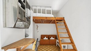 Ein kleines Zimmer mit Etagenbett, Holzschreibtisch, einer Hockerleiter und einer kleinen Sitzecke.