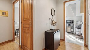 A hallway with wooden doors, a small cabinet, and a kitchen area visible through an open door. - Warm Apartment - Montmartre - Mobility Lease (Paris)