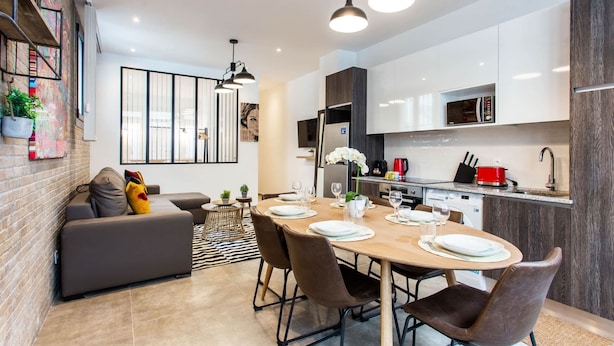 Een moderne keuken met witte kasten, een eethoek met een houten tafel en een grijze bank.