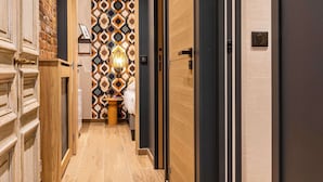 Um corredor com piso de madeira, parede estampada e porta com luminária.