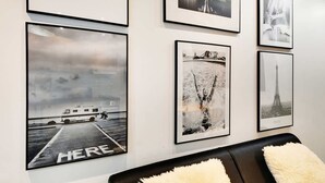 Eine Wand mit gerahmten Schwarz-Weiß-Fotos, darunter ein Boot an einem Steg und der Eiffelturm.