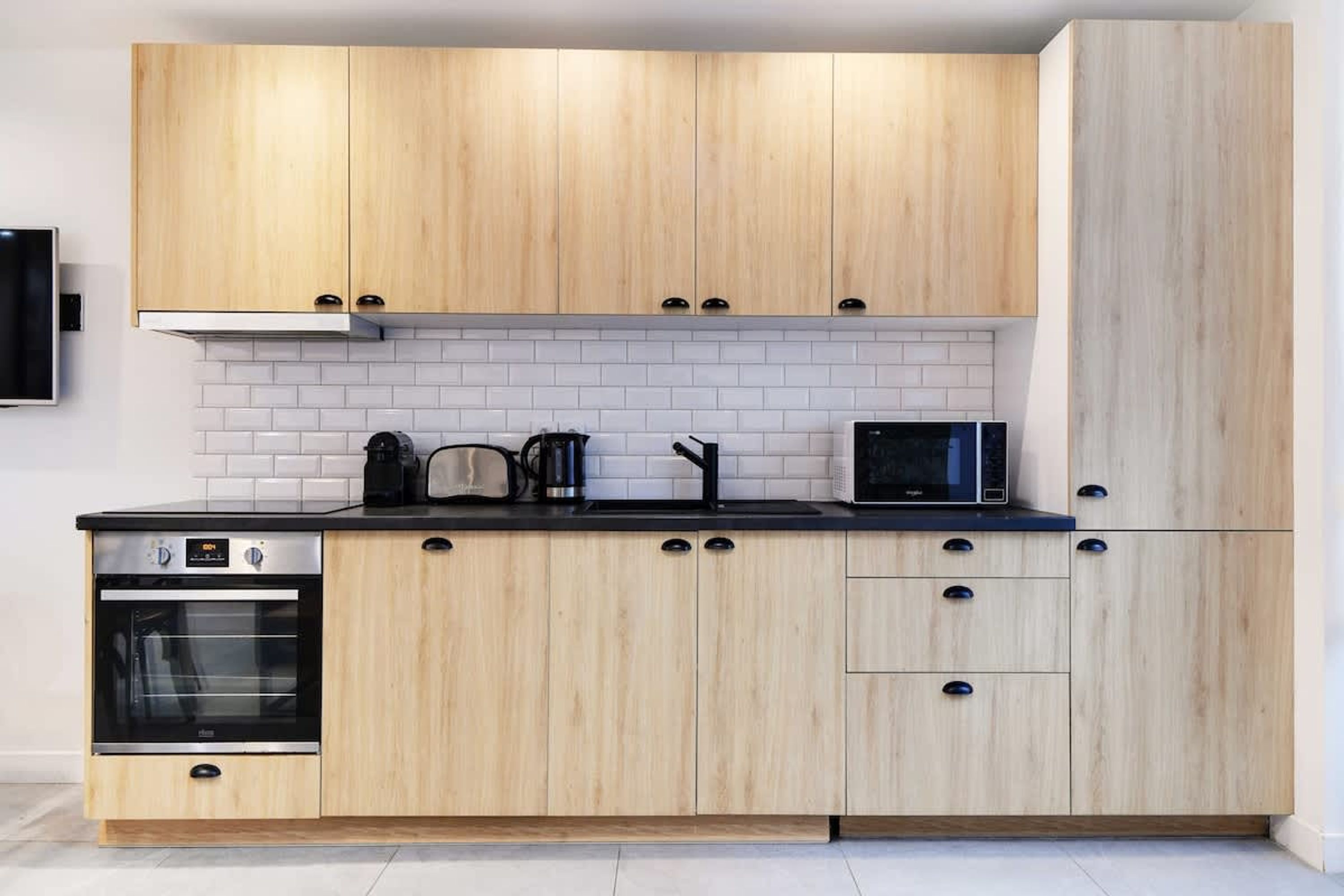 A modern kitchen with light wood cabinets, a black countertop, a built-in oven, a microwave, and a coffee maker.