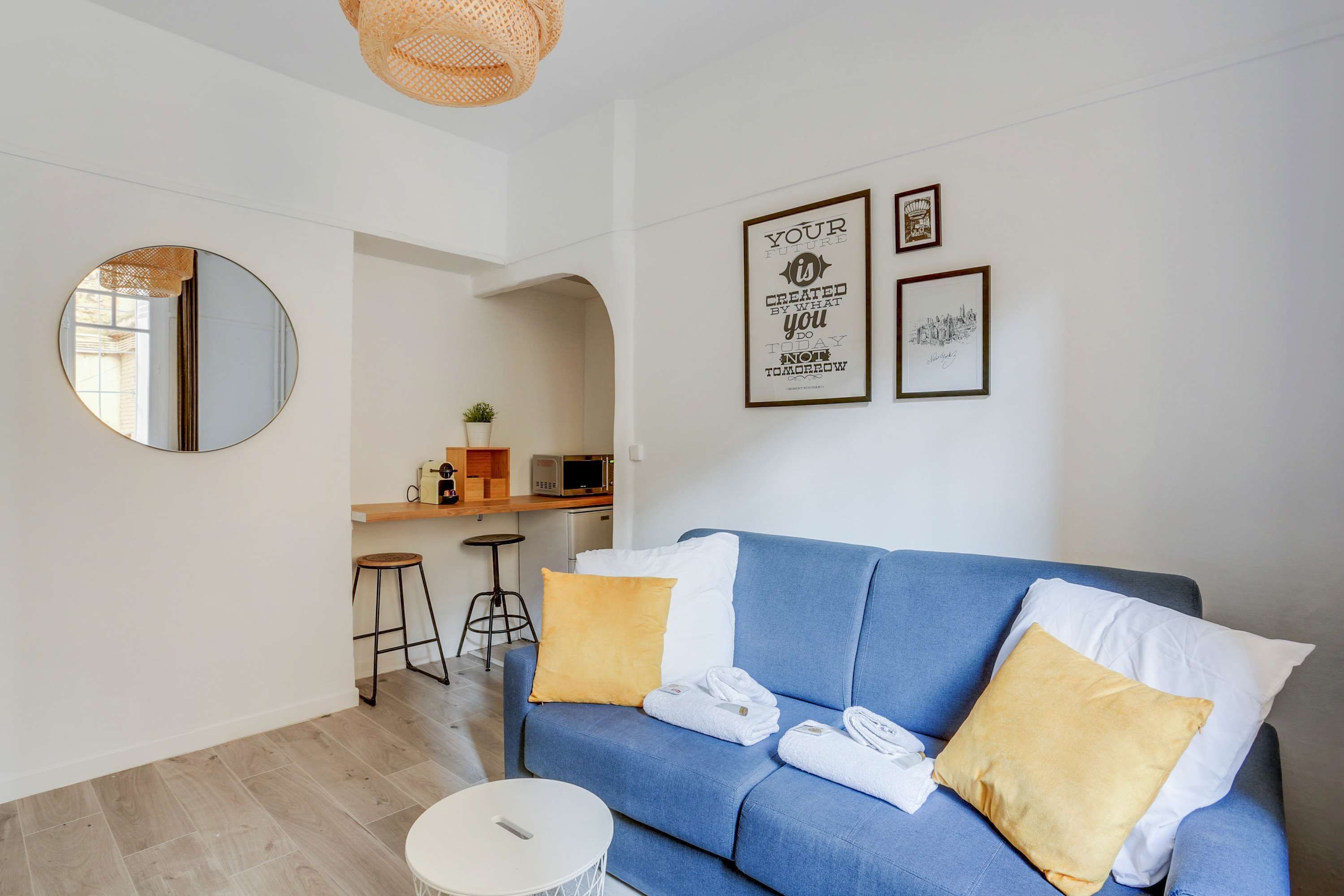 A modern living room with a blue sofa, two yellow pillows, a round mirror, and a small round table.