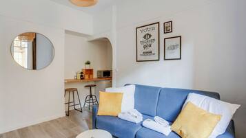 A modern living room with a blue sofa, two yellow pillows, a round mirror, and a small round table.